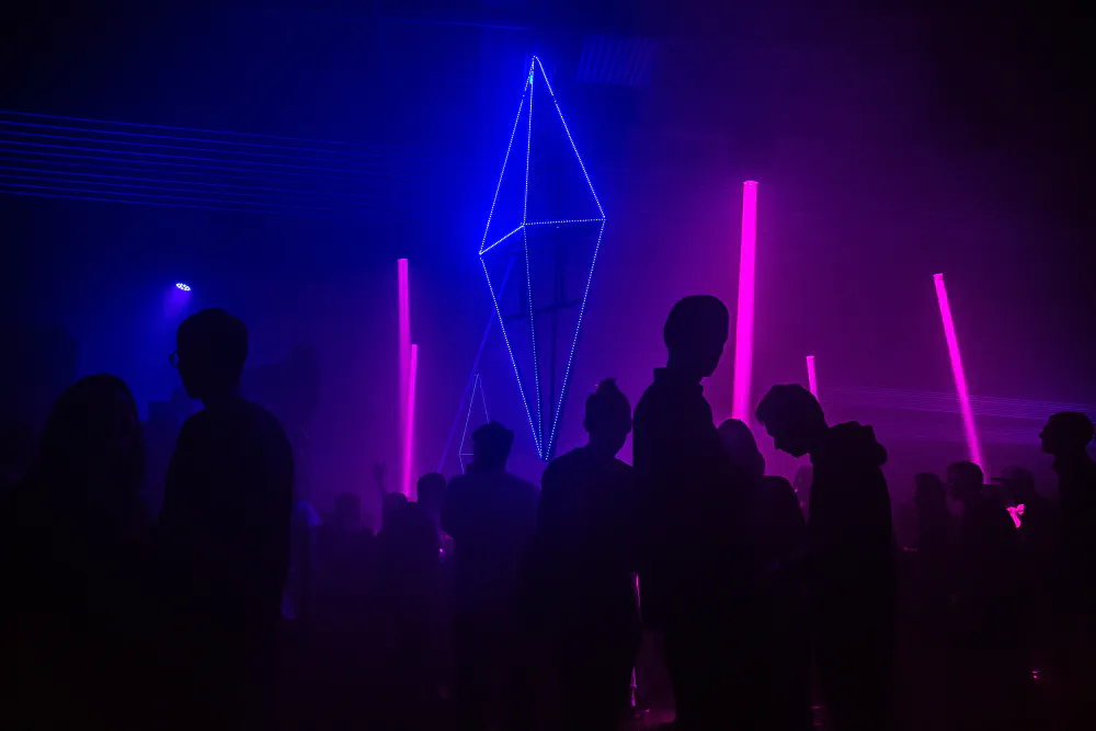 Silhouettes of a crowd in a nightclub, a couple of pink and blue strobes in the back